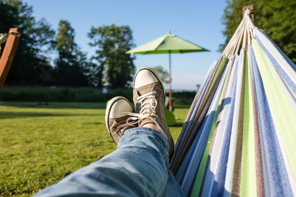 Feet in sneakers and jeans in a hammock, camping, against the backdrop of a summer landscape. Lifestyle. - Φωτογραφία, εικόνα