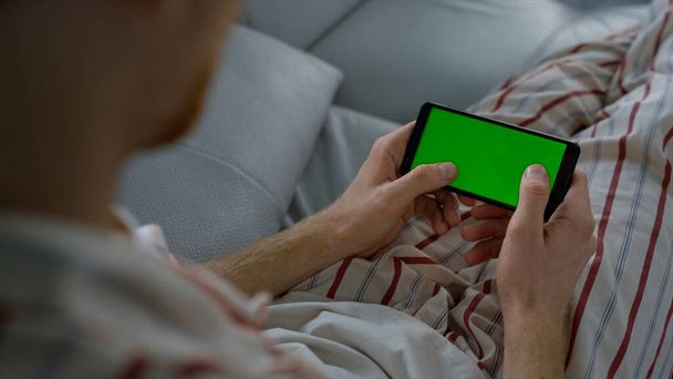 Mann tippt grünen Bildschirm auf Smartphone zu Hause. Spieler genießen Online-Spiel Nahaufnahme. Unbekannter hält Smartphone-SMS im Internet auf Handy fest. Unbekannter benutzt Handy-Attrappe. - Foto, Bild