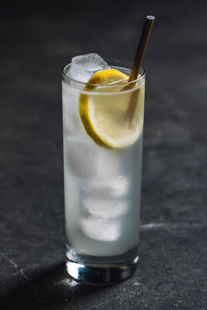 tom collins soda water cocktail in tall glass with lemon wheel, ice, gold drinking straw - Foto, afbeelding
