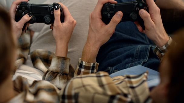 Players hands holding gamepads resting home closeup. Couple enjoy video game. Unrecognized students man woman using joysticks pushing buttons combination. Excited friends playing console together. - Photo, Image