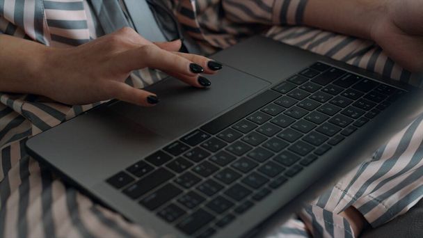 Dziewczyna z bliska za pomocą laptopa przeglądającego internet w piżamie. Ręczne dotykanie poduszki urządzenia wyszukiwania informacji. Nierozpoznana praca przy tworzeniu projektu na komputerze w biurze domu. Koncepcja kształcenia zdalnego. - Zdjęcie, obraz
