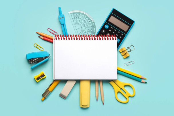 Top view of spiral notepad and school supplies with space for text on blue background. Back to school concept - Photo, Image