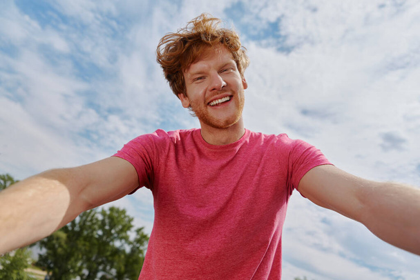Handsome young redhead man making selfie and smiling while standing outdoors - Fotoğraf, Görsel