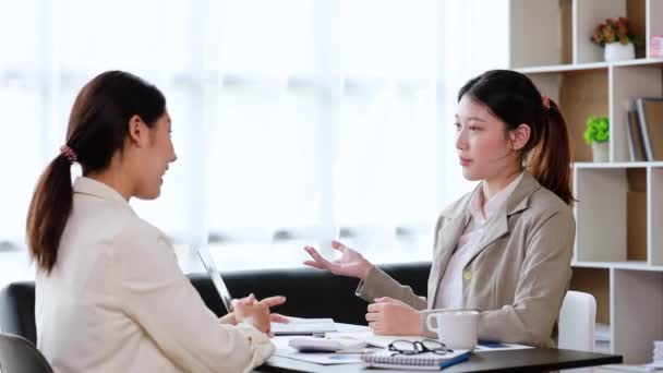 Two women sitting through white papers and talking, two business women discussing brainstorming and planning operations, form a partnership to form a startup company. Management of startup company. - Video, Çekim