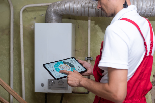 De technicus controleert het verwarmingssysteem in de stookruimte met tablet in de hand - Foto, afbeelding