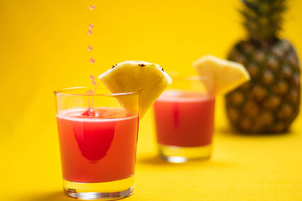 Pineapple juice in glass closeup near sliced fruit with spash and dripping liqid for summer vibes. Healthy organic beverage on an orange background, copyspace. - Φωτογραφία, εικόνα