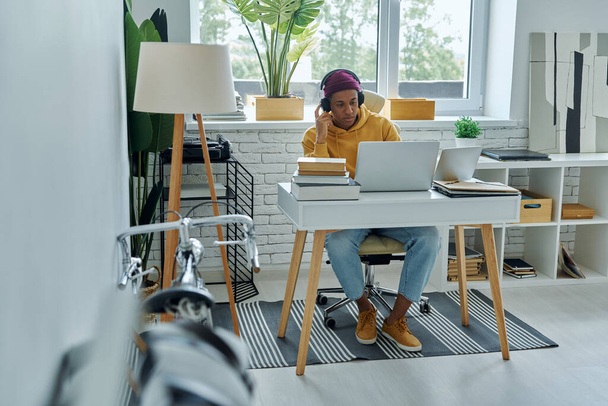 Concentrated African man in headphones using laptop while working in office - Photo, image