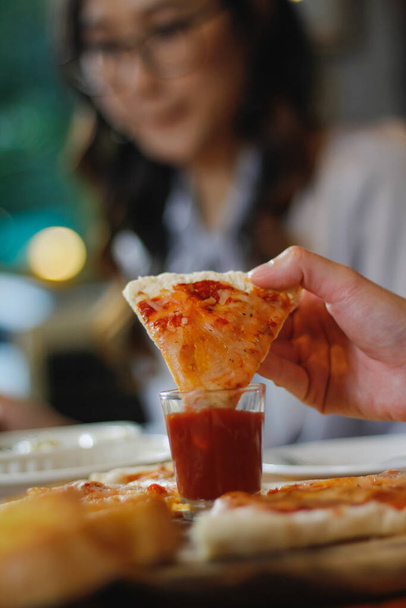 Μια νεαρή γυναίκα είναι στην ευχάριστη θέση να δείτε το φαγητό στο τραπέζι και να επιλέξετε το μενού πίτσα για να φάει με καλό γούστο. Pizza μενού είναι ιδανικό για δεξιώσεις μεταξύ φίλων και της οικογένειας, όπως είναι άνετα να φάει - Φωτογραφία, εικόνα