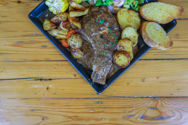 Gegrilde biefstuk met jus wordt geserveerd met een groente- en fruitsalade in een zwarte keramische plaat op de eettafel om de biefstuk te bereiden voor een feestelijk diner. - Foto, afbeelding