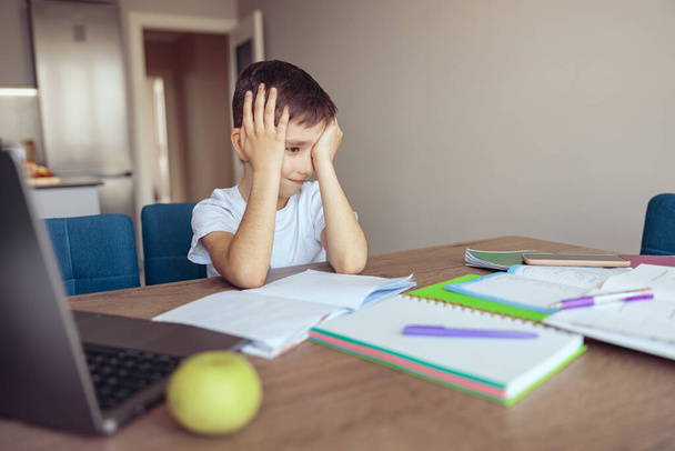 Väsynyt surullinen pieni koulupoika istuu vaikeissa kotitehtävissä kotona ja itkee. Verkko-oppiminen Tutkimus. - Valokuva, kuva