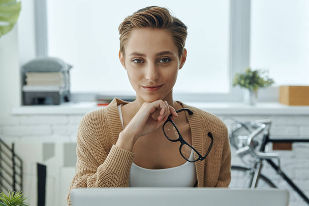 Confident young woman looking at camera while sitting at her working place in office - Photo, image