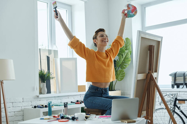 Happy young woman keeping arms outstretched while spending time in art studio - 写真・画像