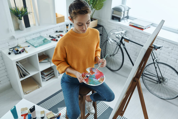 Top view of beautiful young woman mixing colors while drawing in art studio - Фото, изображение