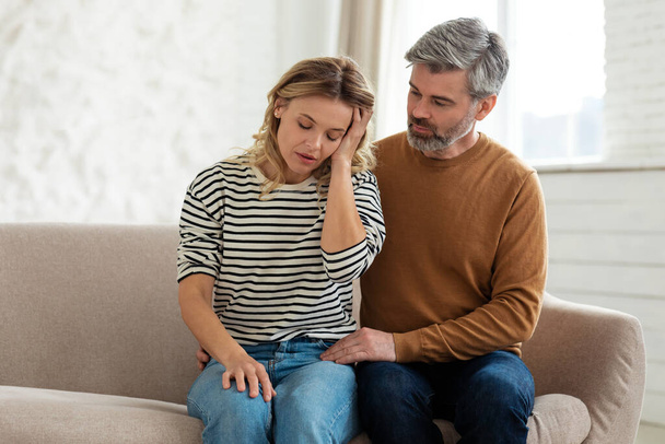 Päänsärky Aviomies tukee vaimo kärsii kivulias migreeni koskettava pää istuu sohvalla kotona. Hypertensio-oire, naisten terveysongelmat käsite - Valokuva, kuva
