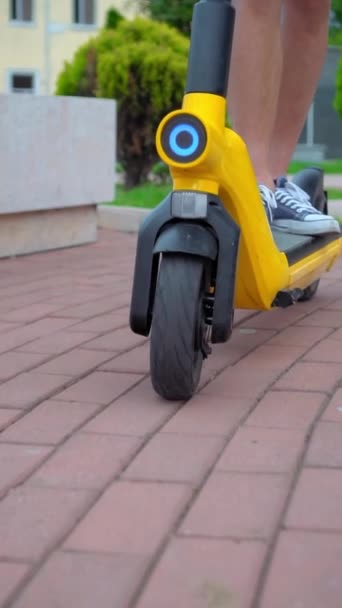 Close-up of men's feet in sneakers, riding through streets of city and in park on electric scooter or scooter. Vertical video, slow motion. Yellow and black. Ecological and mobile transport in city. - Footage, Video