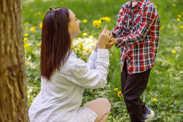 Beautiful mother getting flowers from small son in park. Woman with dandelions from kid. Nature. - Photo, Image