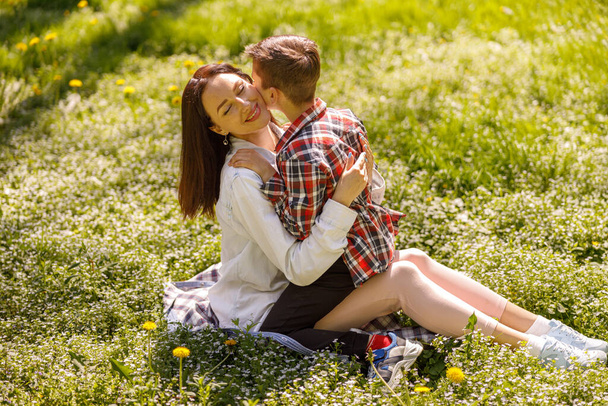Hermosa mujer caucásica sentada sobre hierba verde y sosteniendo pequeño hijo lindo. Día de verano. Afuera.. - Foto, imagen
