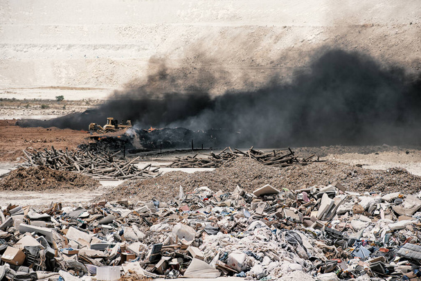 Fire at garbage dump. Black smoke from burning old tyres and bulldozer fighting fire - Photo, Image