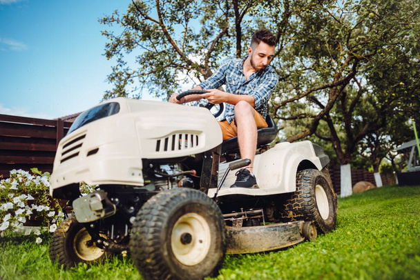 Man using lawn tractor for mowing grass in garden. Landscaping works with professional tools - 写真・画像