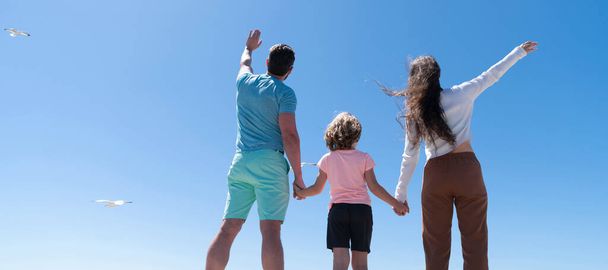 A család zászlaja ölelkezik a tengerparton. Nyári családi nyaralás, vízszintes transzparens. Anya apa és fia keres a jövőben kéz a kézben nyáron, visszapillantás, szeretet - Fotó, kép