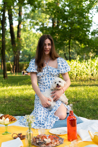 a girl on a picnic holds a dog in a blue dress. In the park - Fotó, kép