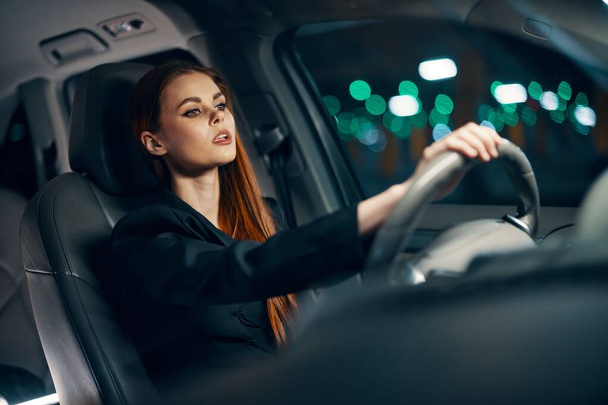 foto horizontal de uma mulher bonita em uma camisa preta dirigindo um carro enquanto dirige à noite. Foto de alta qualidade - Foto, Imagem