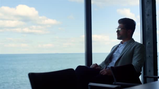 Молодой бизнесмен смотрит в панорамное окно. Тщательный человек рассматривает проблемы с видом на море. Стрессовый парень думает о принятии будущих решений. Заинтересованный клиент ждет менеджера адвоката в одиночку. - Кадры, видео