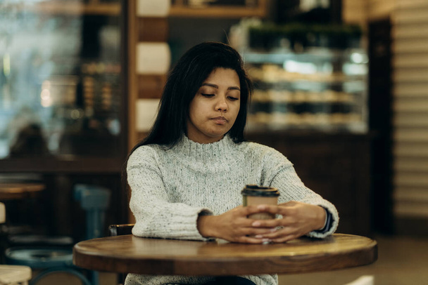 Afroamerikkalainen nainen kahvilassa puhumassa puhelimessa ja juomassa kahvia. Tummaihoinen nuori nainen istuu kahvilassa ja juo kahvia odottaessaan kumppaniaan.. - Valokuva, kuva