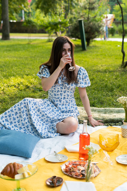девушка в синем платье в парке на пикнике на отдыхе пьет вино - Фото, изображение