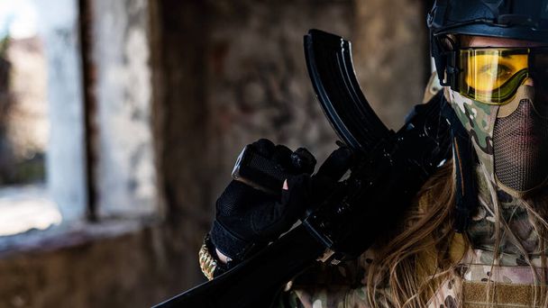 Portrait of a woman in a helmet and goggles with a machine gun in her hands. A female soldier in a camouflage uniform holds a weapon - Foto, imagen