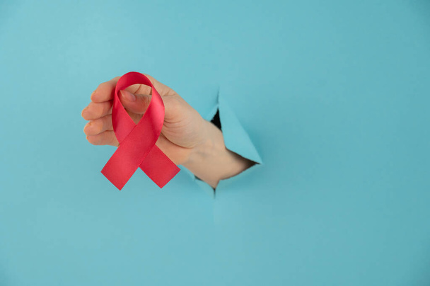 A womans hand with a red bow sticks out of a hole in a blue background. Symbol of the fight against AIDS - Fotoğraf, Görsel