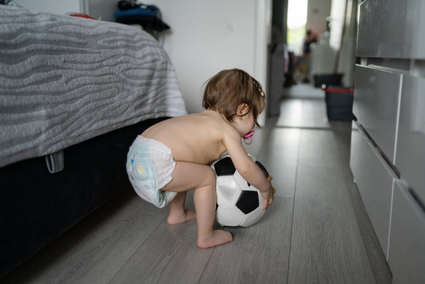 Ein Mädchen Kleinkind kaukasischen Kind hält Fußballball zu Hause ohne Kleidung Frühe Entwicklung Lernen und Spielkonzept echte Menschen kopieren Raum - Foto, Bild