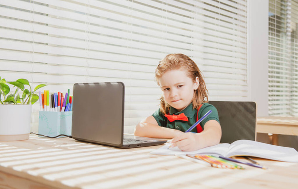 Cute school boy child does her homework with a tablet or laptop at home. Pupil writes the task in a notebook. Education and learning, kids home schooling - Foto, imagen