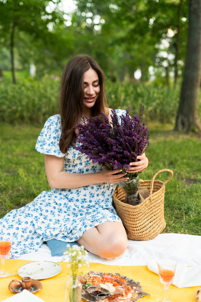 young girl in a blue dress holding lavender at a picnic in nature - Fotó, kép