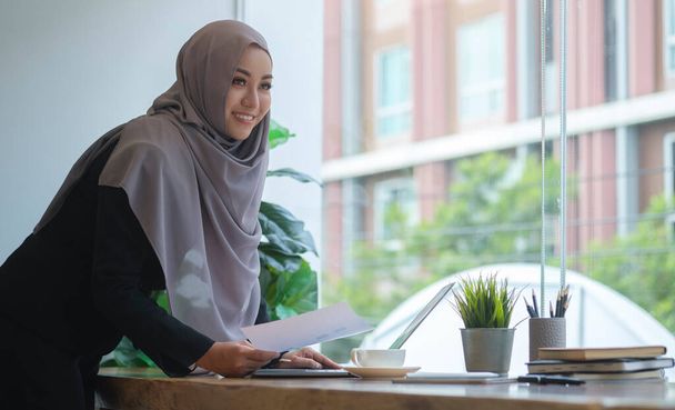 Successful young muslim female corporate CEO planning investment strategy for startup project, working with financial document at office. - 写真・画像