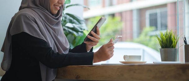 Smiling muslim woman in hijab holding credit card for online shopping or payment online on smart phone. E-commerce, internet banking concept. - Foto, Imagem