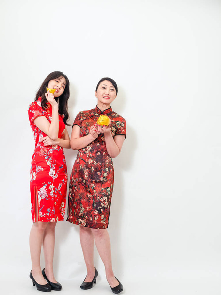 Portrait of asian young woman and elder woman both wearing traditional cheongsam qipao dress showing Gold ingot and pig meaning "May wealth come generously to you" on white background. - Foto, afbeelding