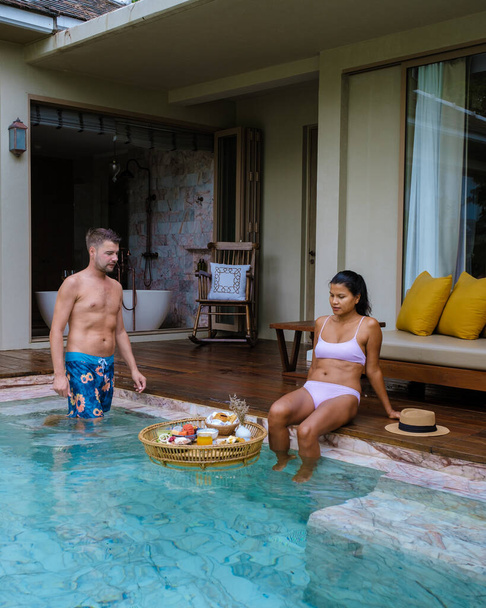 Пара чоловіків і жінок снідали в басейні на віллі басейну під час відпустки. подружжя під час розкішної відпустки в Таїланді, плаває сніданок. - Фото, зображення