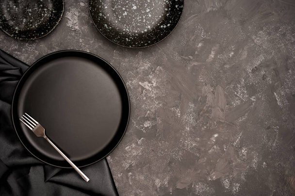Концепция керамической ручной работы. Пустые черные керамические плиты на черном фоне обеденного стола. вид сверху - Фото, изображение