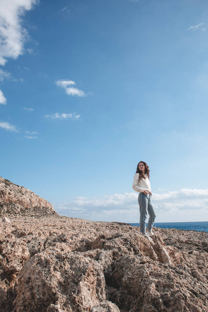Young woman is standing on the land desert ground in front of the mountain Cape Greco in Ayia Napa, Cyprus.  - Fotó, kép