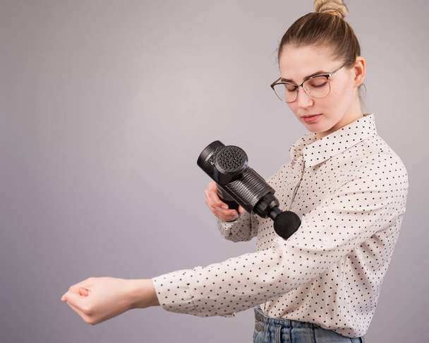 Caucasian business woman massaging her biceps with a percussion massager - Foto, Imagem