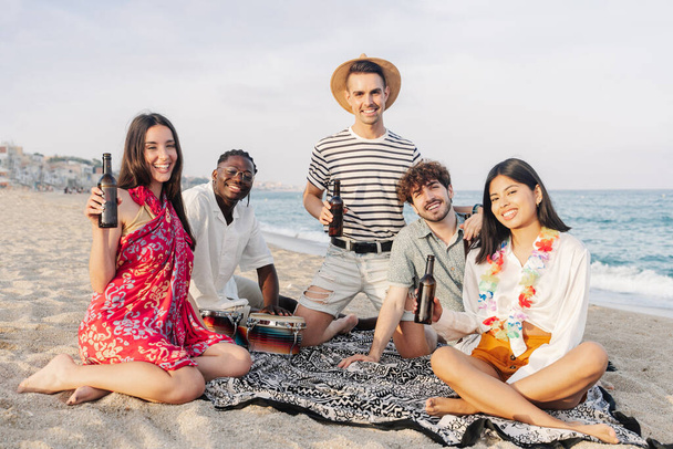 Gruppe multikultureller Freunde sitzt am Strand beim Sommer-Musikfestival - Foto, Bild
