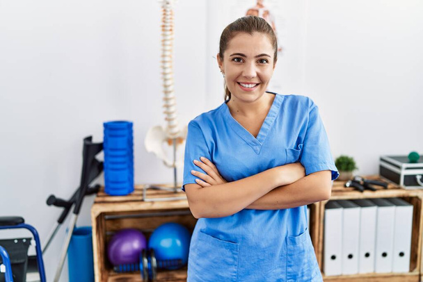 Nuori latino nainen yllään fysioterapia univormu seisoo kädet ristissä ele urheilukeskus - Valokuva, kuva