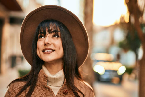 Brunette woman wearing winter hat smiling outdoors at the city - Photo, Image