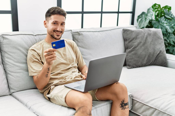Young hispanic man using laptop and credit card at home - Foto, Bild