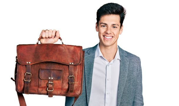 Young hispanic man holding business bag looking positive and happy standing and smiling with a confident smile showing teeth  - Foto, afbeelding