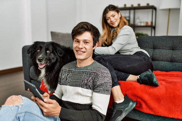 Jovem casal caucasiano sorrindo feliz com o cão usando touchpad em casa. - Foto, Imagem