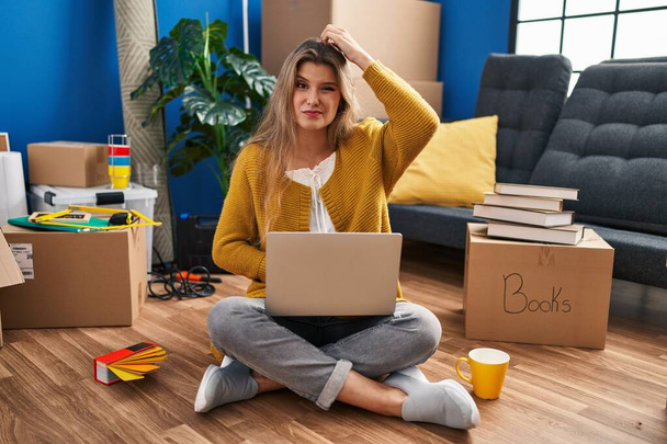 Fiatal nő ül a padlón az új otthon segítségével laptop zavaros és csoda kérdés. bizonytalan a kétség, gondolkodás kéz a fejen. elmélkedő koncepció.  - Fotó, kép