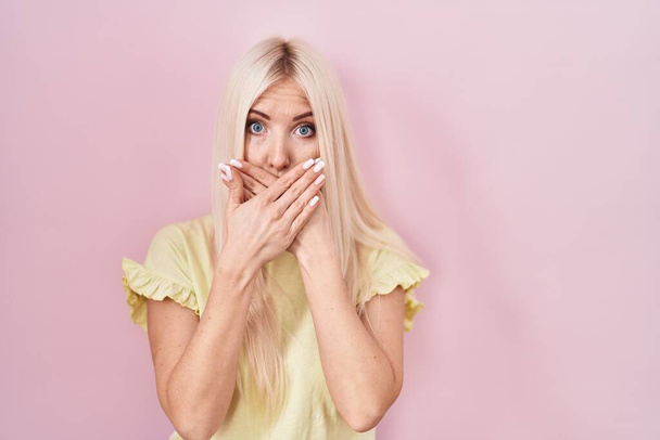 Kaukasische Frau steht über rosa Hintergrund schockiert bedeckt Mund mit den Händen für Fehler. Geheimes Konzept.  - Foto, Bild