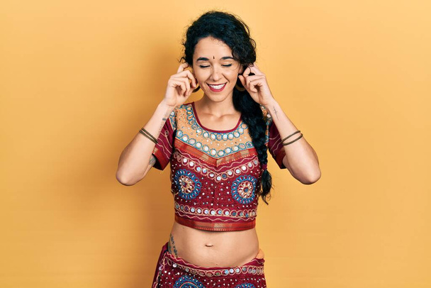 Young woman wearing bindi and bollywood clothing covering ears with fingers with annoyed expression for the noise of loud music. deaf concept.  - Foto, afbeelding